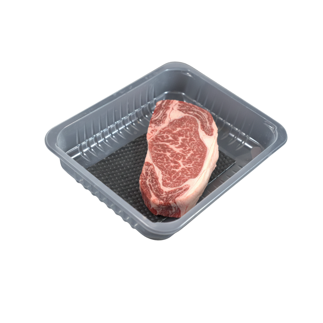 Axorbia Meat Pad under a ribeye steak in a black packaging tray